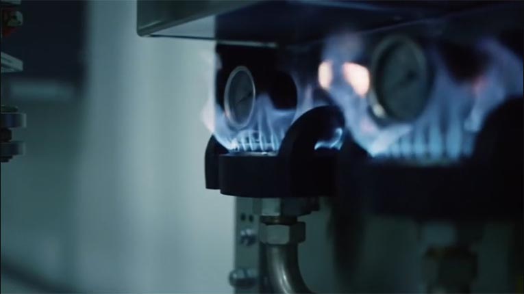 Close‑up of a high‑efficiency boiler’s modulating gas burner with blue flames and pressure gauges.