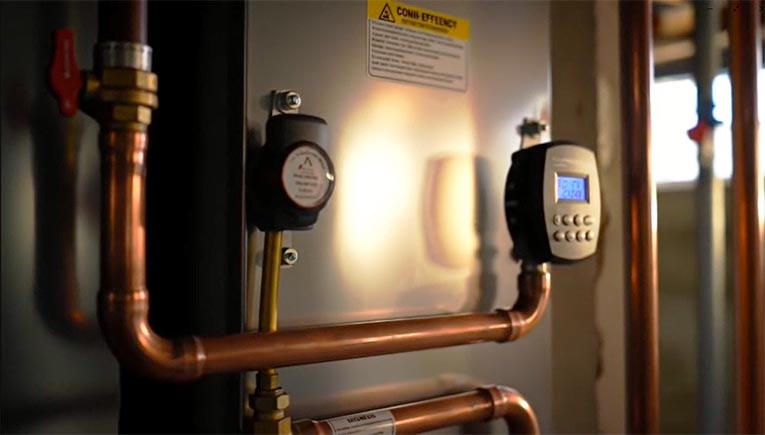 Close‑up of a high‑efficiency boiler’s copper piping, pressure gauge, and digital control panel indicating operating status.