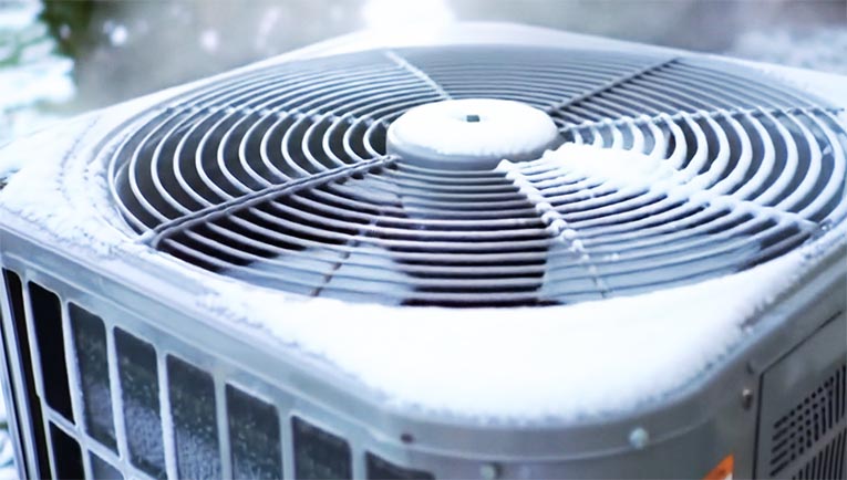 Snow-dusted outdoor heat pump in Denver during defrost cycle
