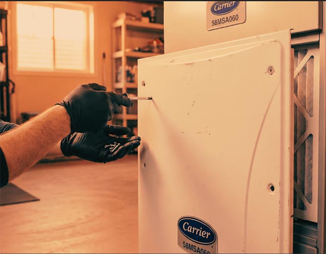 An HVAC technician secures the access panel on a Carrier 58MSA060 furnace after changing the filter and doing annual maintenance.