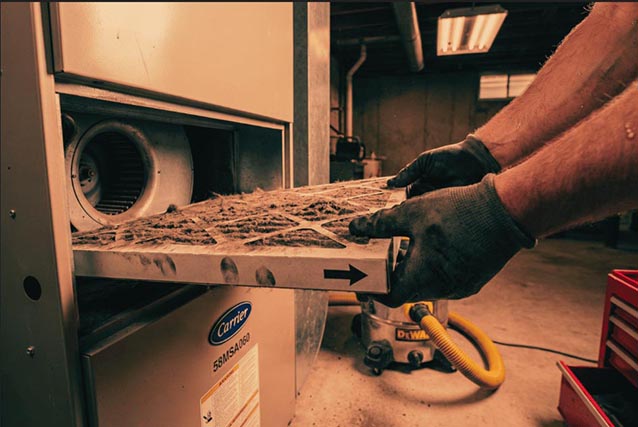 Hands removing heavily soiled furnace filter from Carrier 58MSA060 showing dust buildup and directional airflow arrow.