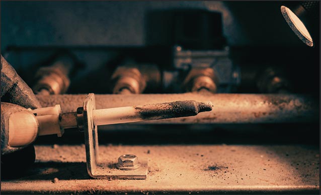 Close-up of flame sensor rod with black soot buildup inside Carrier furnace burner compartment requiring cleaning.
