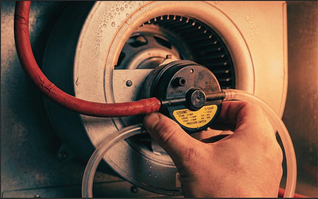 An HVAC technician is checking the pressure switch on the Carrier 58MSA060 draft inducer motor housing with red hoses.